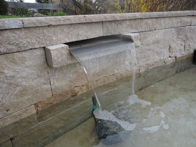 breiter Wasserauslass an Travertinbrunnen aus Mauersteinen