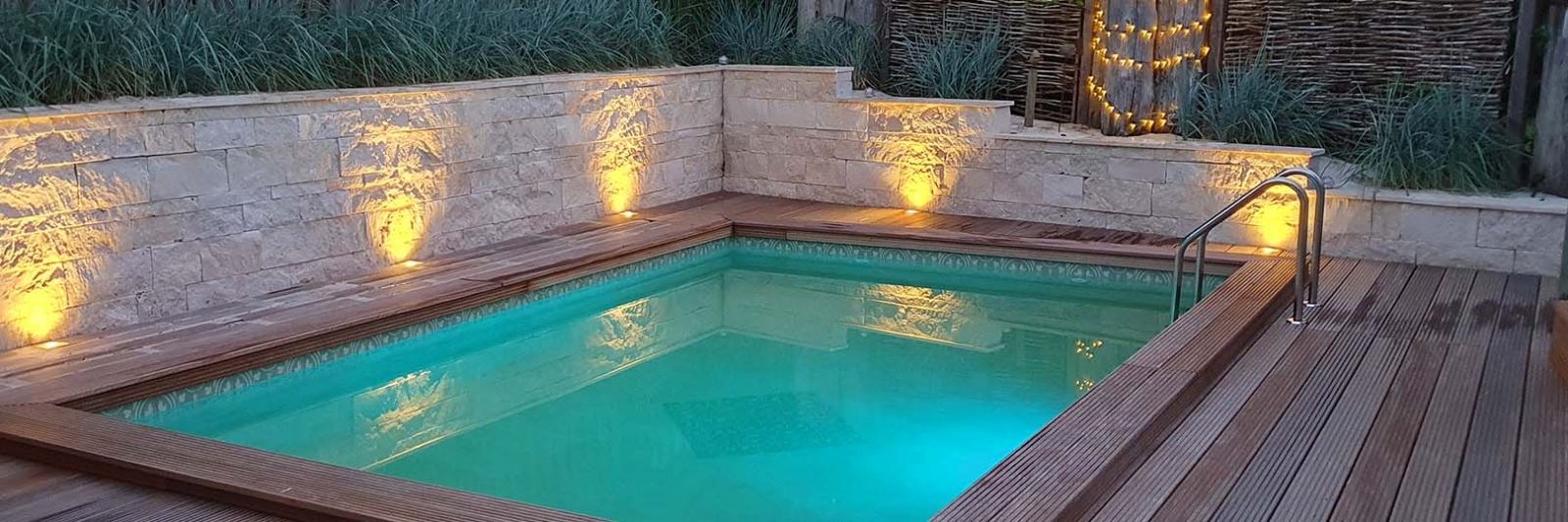 Mauer aus beigem Travertin am Pool mit Beleuchtung am Abend