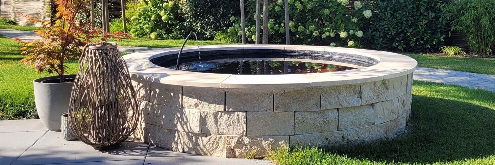 runder Brunnen gebaut aus hellbeigen Travertin Mauersteinen